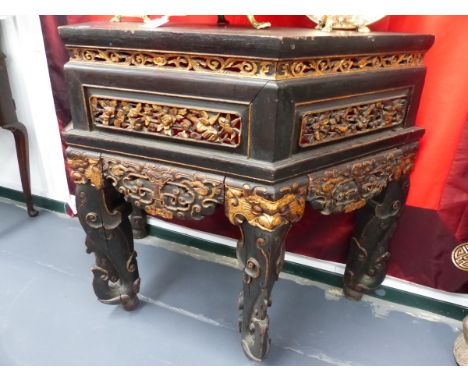 A CHINESE GILT AND EBONISED CARVED ALTAR TABLE WITH SHAPED TOP ABOVE PANELLED FRIEZE SCROLL LEGS.   H.89 W.114 D.47cms.