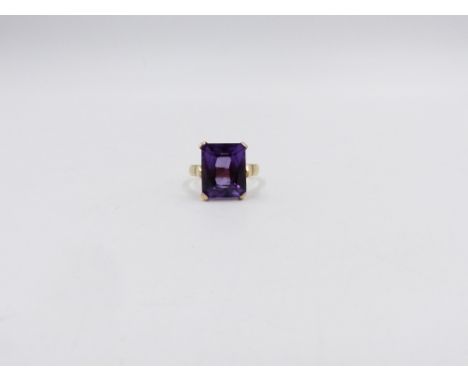 AN 18ct STAMPED YELLOW GOLD PURPLE SAPPHIRE DRESS RING. THE CENTRAL PURPLE SAPPHIRE IS AN EMERALD CUT WITH A FOUR CLAW SETTIN