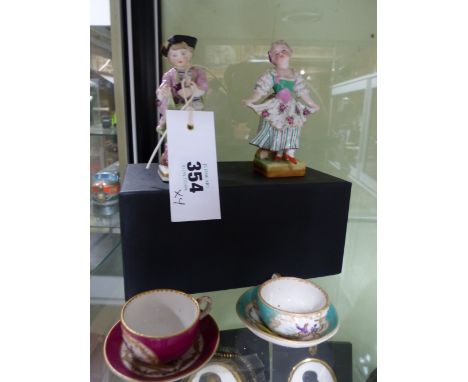 TWO POLYCHROME PORCELAIN FIGURES OF A BOY AND GIRL IN THE MANNER OF MEISSEN AND TWO MINIATURE CUPS AND SAUCERS.