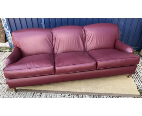 A modern burgundy leather upholstered three seat sofa in the manner of Howard of London on turned and stained beech front leg
