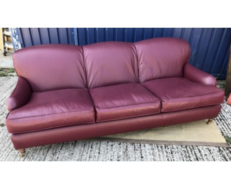 A modern burgundy leather upholstered three seat sofa in the manner of Howard of London on turned and stained beech front leg
