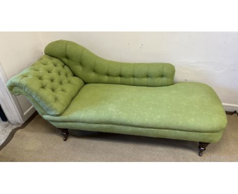 An Edwardian chaise longue with button back upholstery raised on ringed and turned front legs to brass caps and china castors