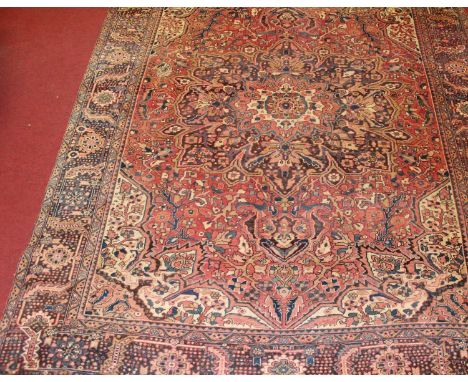 A Persian woollen Heriz carpet, the red ground having a central medallion issuing scroll flowers and foliage within trailing 