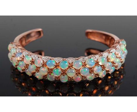 A rose metal torque bangle, comprising three rows of hydrophane opal cabochons, 41 in total, within a border of 28 single cut