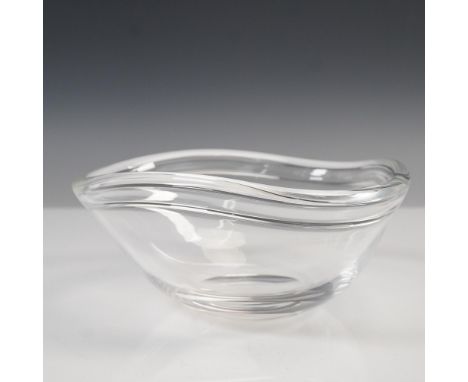 A clear glass bowl featuring a rounded triangular form with soft, curved edges. The bowl is accompanied by its original Steub