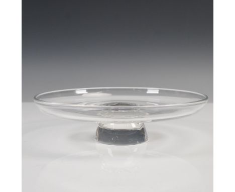 A clear crystal round serving tazza featuring a wide, flat tray supported by a raised pedestal base. The base is adorned with