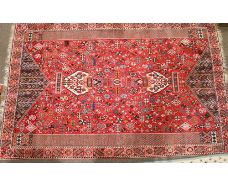 A Persian style woollen rug on a red ground. Multiple geometric borders. Traditional stylized motifs. 254cm x 162cm