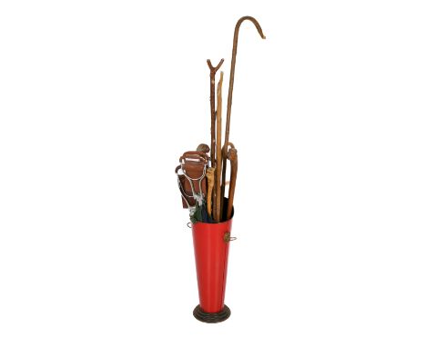 A red metal stick stand containing an assortment of walking and shooting sticks. The stand of cylindrical form with lion head