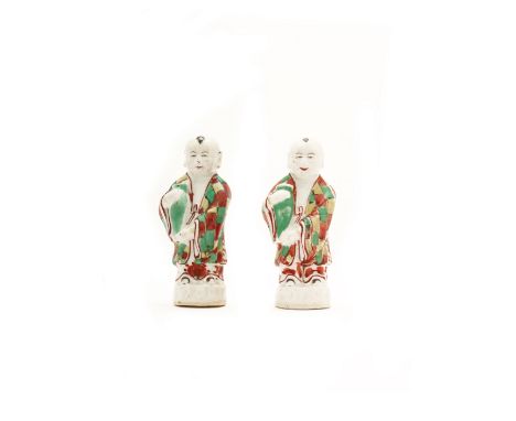 A pair of Chinese wucai taper holdersQing dynasty, Kangxi periodModelled as boys holding jars in their arms, glazed in red an
