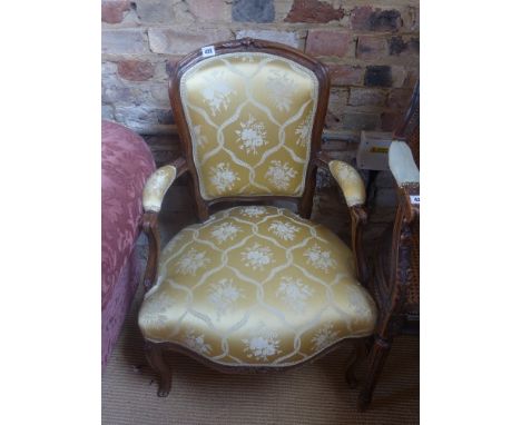 A French style walnut framed open armchair with gold upholstered back padded arms and overstuffed seat raised on cabriole sup