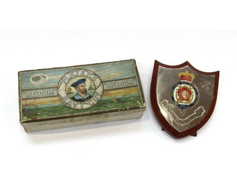 An HM Yacht Britannia badge on easel-backed shield and a vintage Players Navy Cut box (2)