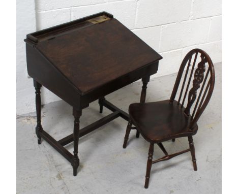 An early 20th century oak child's desk with ceramic ink pots and brass covers, to turned tapering supports and cross stretche