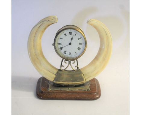 BOAR TUSK MANTLE CLOCK a mantle clock with a white enamel dial, in a metal case and mounted on a stand with two Boar Tusks on