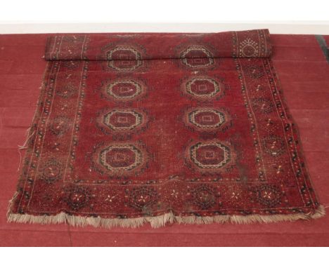A vintage Bokhara red ground wool rug. Length: 195cm, W: 126cm.  Condition fair. Rug is worn in places with a patch of dirt i