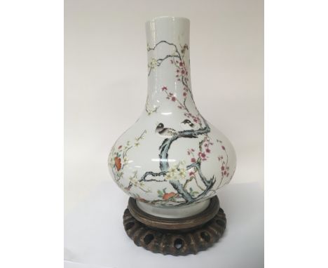 A Chinese porcelain bottle vase enamel decorated with flowers foliage and birds caricature marks to the base on a hardwood st