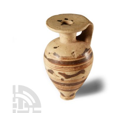 8th-7th century B.C. With a piriform body and narrow foot, deep shoulder and flange rim, strap handle to the rear; the rim an