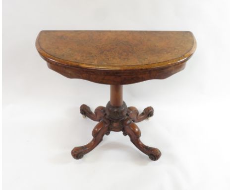 A Victorian inlaid burr walnut demi lune fold over card table on rounded pillar and four outswept supports with decorative fo