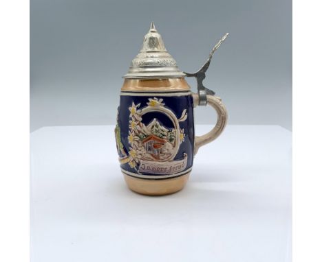 A small ceramic beverage mug with a pewter lid, decorated with a raised design of two men, German scenery and flowers. Dimens