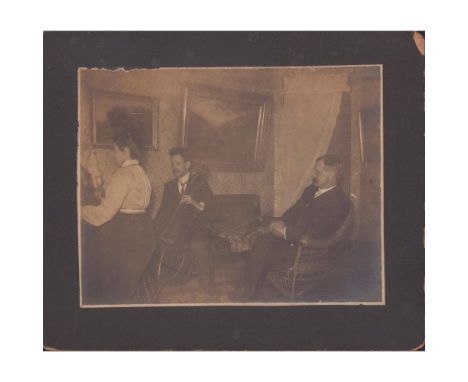 An indoor photo of a seated man watching a woman on the piano, and another man playing the cello. Board size: 6in x 5in. Sigh