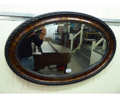 A 1930s mirror, the oval bevelled plate set in a walnut finished and painted carved wooden frame  16'' x 26''      LSF