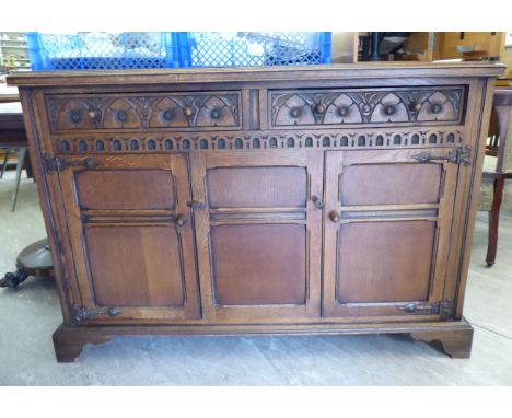 A mid 20thC carved oak sideboard with a low upstand, two in-line drawers and a pair of twin panelled doors, raised on a brack