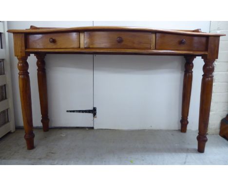 A modern honey coloured hardwood serpentine front hall table with a low galleried back and three in-line frieze drawers, rais
