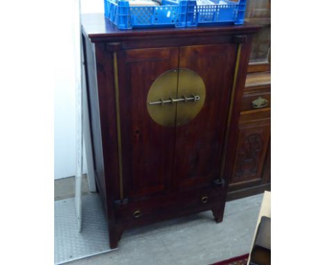 A modern Chinese design dark stained hardwood cabinet with burnished iron fittings, the two doors over a base drawer, raised 