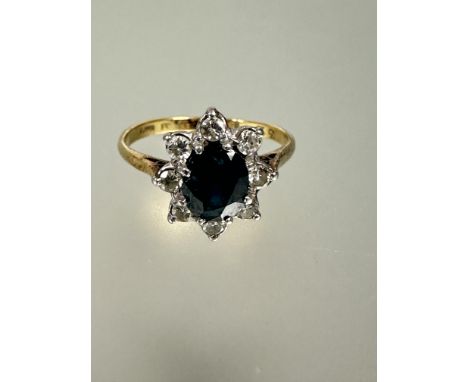 A 18ct gold and platinum set sapphire and diamond cluster ring the oval faceted sapphire approximately 0.75ct within a surrou