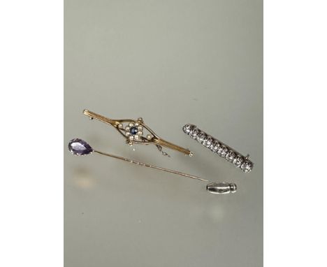 A Edwardian 15ct gold bar brooch set central sapphire within a surround of eight half seed pearls flanked by a seed pearl com