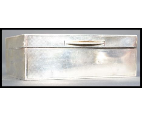 An early 20th century silver hallmarked cigarette box humidor having an engine turned design with plain cartouche panel to li