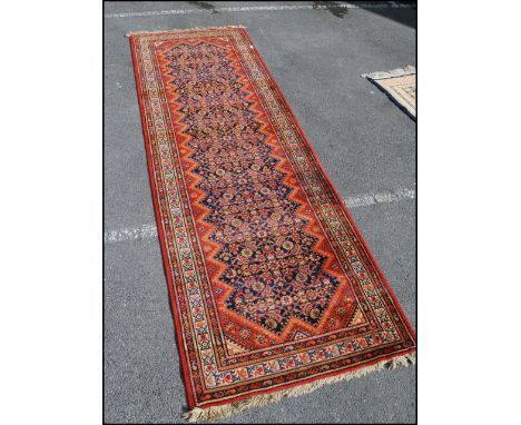 A vintage early 20th century Persian / Islamic long runner rug carpet of woolen construction having a decorative red ground w