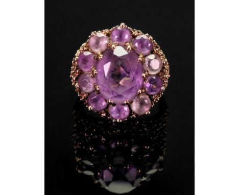 A 9ct amethyst-set dress ring of cluster design, the central oval-cut amethyst claw-set with a surround of circular-cut ameth
