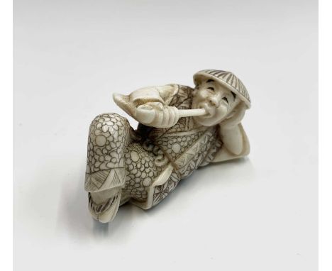 A Japanese ivory netsuke, early 20th century, modelled as a recumbent male smoking a pipe, height 2.5cm, width 4.8cm, depth 2