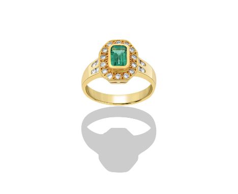 An 18 Carat Gold Emerald and Diamond Cluster Ringthe emerald-cut emerald in a yellow rubbed over setting, within a border of 