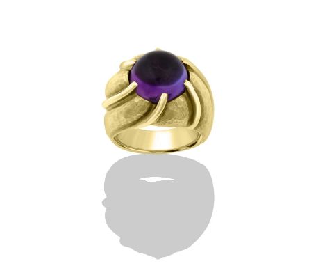 An Amethyst Ringthe round cabochon amethyst in a yellow claw setting, the claws extending into the planished motif shoulder, 