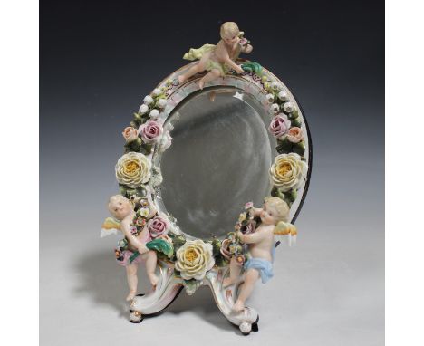 A Sitzendorf porcelain floral encrusted mirror frame, late 19th century, of oval shape, applied with three cherubs holding fl