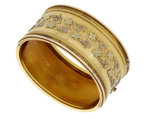A gold bangle, circa 1870, the front with applied ivy leaf and flowerhead decoration, the border with bead and ropetwist deta