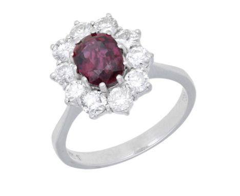 An 18ct white gold ruby and diamond cluster ring, 1977, the oval mixed-cut ruby claw-set within a surround of brilliant-cut d