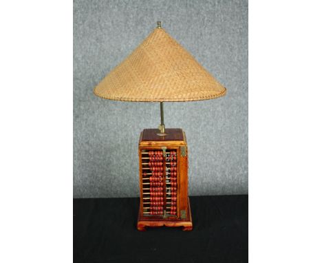 A table lamp fashioned from a four-part abacus with a woven rice picking hat type shade. The abacus with brass fittings, stai