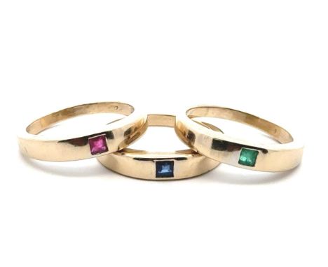 A set of three gold rings stamped 750, each mounted with a square cut gemstone - ruby, sapphire and emerald. Size R