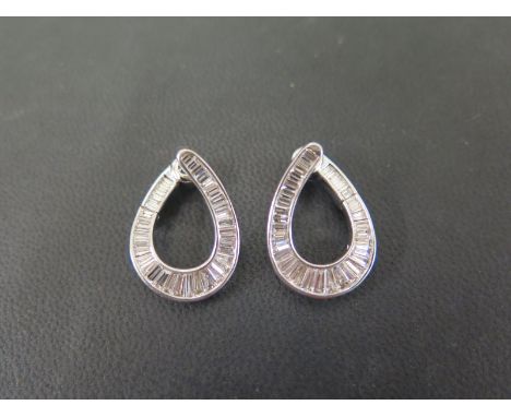 A pair of diamond earrings - Of hoop design the graduated baguette-cut diamonds within a channel setting to the hinged clasp 