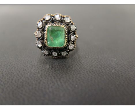 An emerald and diamond cluster ring - The octagonal emerald within a rose-cut diamond surround - Tests as higher carat gold a