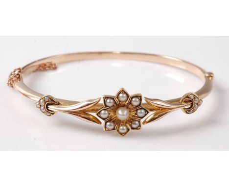 A yellow metal oval hinged hollow bangle with floral detail, set with nineteen 1.5 to 4mm seed pearls, with box clasp and saf