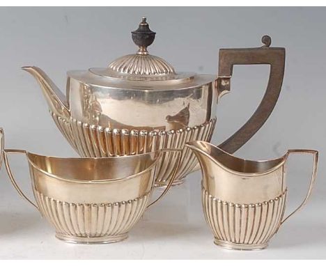 A George V silver three-piece tea set, comprising teapot, twin handled sugar and cream, each of half-reeded oval form, gross 