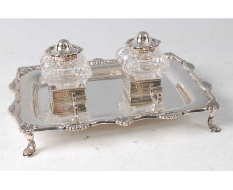 An Edwardian silver desk stand, of shaped rectangular form, with shell capped rim, twin glass inkwells with silver hinged cov