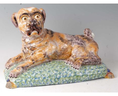 A French faience model of a recumbent pug dog upon a cushion, having all-over sponged decoration (some losses to extremities)