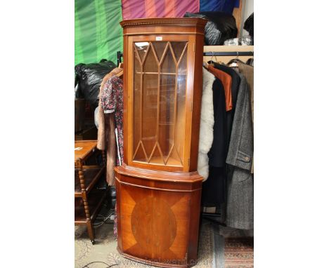 A reproduction Yew finished floor standing Corner Cabinet, having castellated cornice over ten pane glazed door, over single 