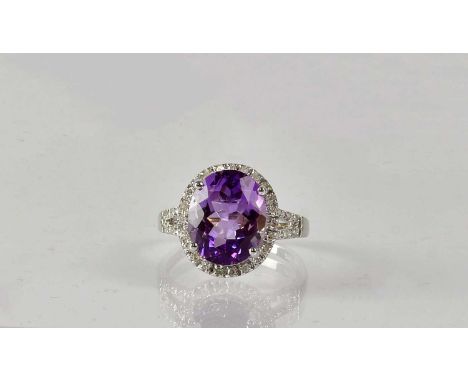 A 14ct white gold ring set with an oval facet cut emerald, in a surround of diamonds, with diamond set open shoulders, stampe