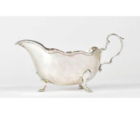 HARRODS LTD; an Elizabeth II hallmarked silver sauce boat with scalloped edge and scroll handle, raised on four hoof feet, Sh