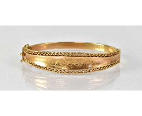 A 9ct yellow gold hinged bangle with safety chain, the front section with pierced border and engraved foliate scrolled vignet